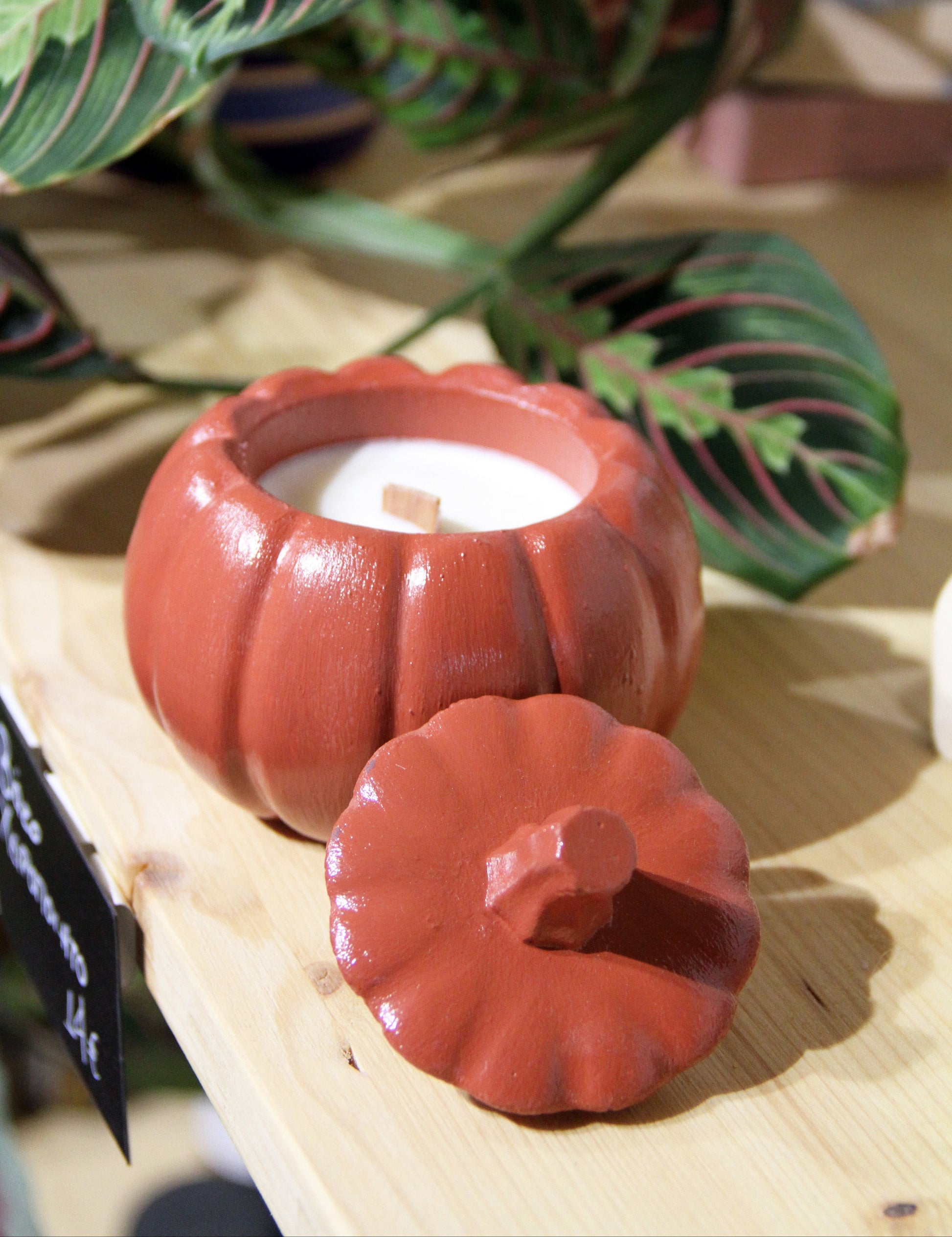Red pumpkin-shaped candle holder with a lit candle on a wooden surface.